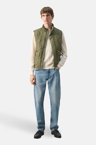 Gilet vert de MANGO, avec surpiqûres en losanges et poches plaquées, porté sur un pull crème et un jean bleu.
