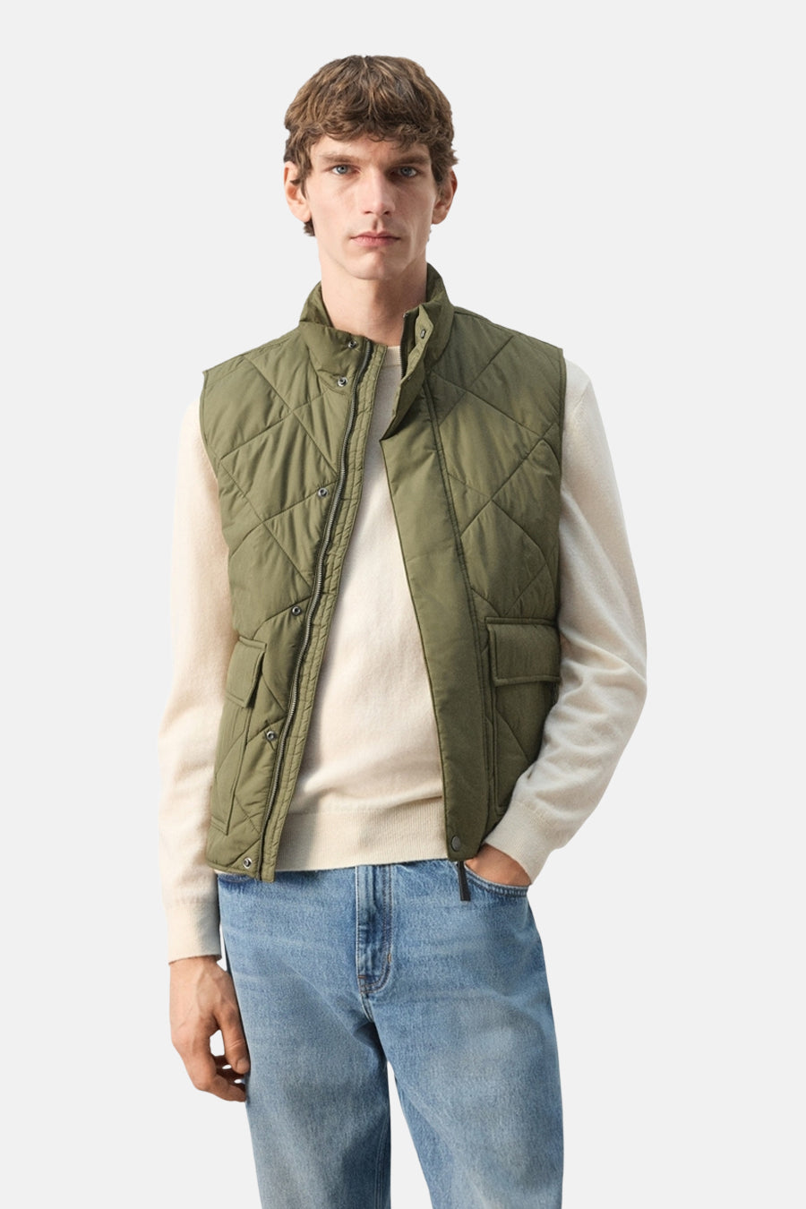 Gilet vert de MANGO, avec un motif matelassé en losanges, porté sur un pull de couleur crème et un jean bleu.