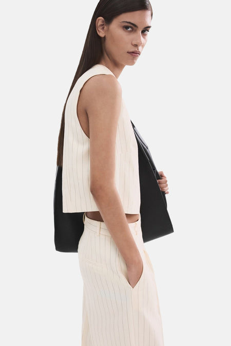 Ecru blouse zonder mouwen van MANGO, met krijtstreep en een zwarte jas nonchalant over de schouder.
