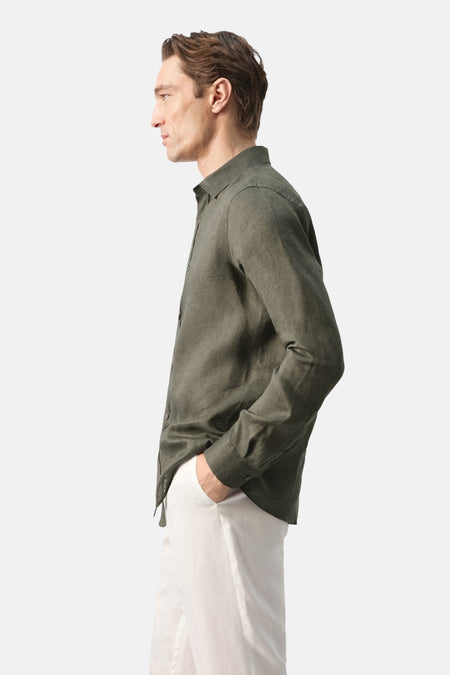Chemise kaki de MANGO, vue de profil, avec manches longues et pantalon blanc.