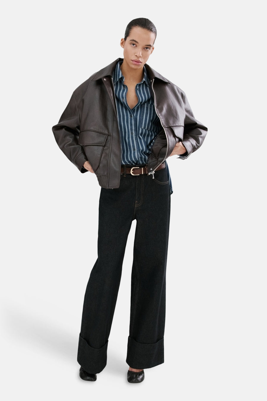 Donkerblauw denim overhemd van MANGO, met verticale strepen en gecombineerd met een bruine leren jas en donkere jeans met omslag.
