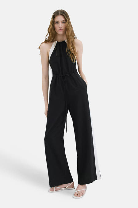 Combinaison noir et blanc de MANGO avec col licou, cordon de serrage à la taille et jambes larges, portée par un mannequin assis.