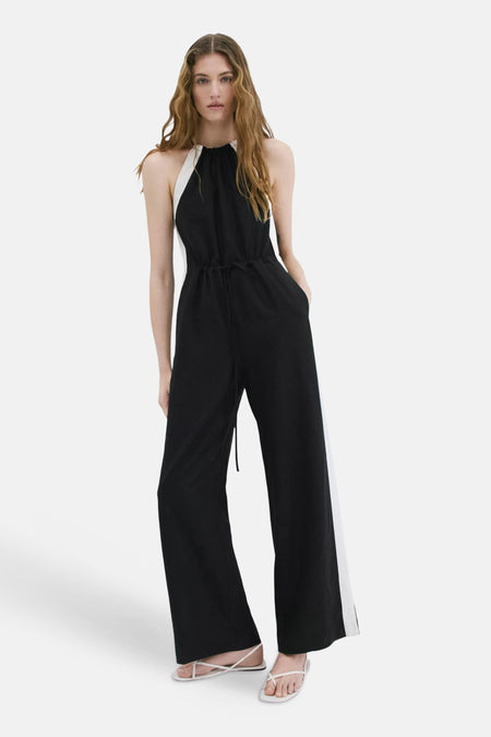 Zwart-witte halterneck jumpsuit van MANGO met trekkoord in de taille, wijde pijpen en witte zijstrepen.