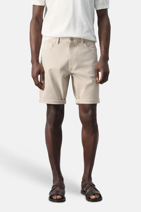 Beige bermuda van MANGO, opgerold bij de zoom, gedragen met een wit T-shirt en donkerbruine sandalen.