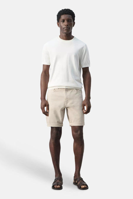 Beige bermuda van MANGO, met opgerolde pijpen, gedragen door man met wit T-shirt en donkerbruine sandalen.