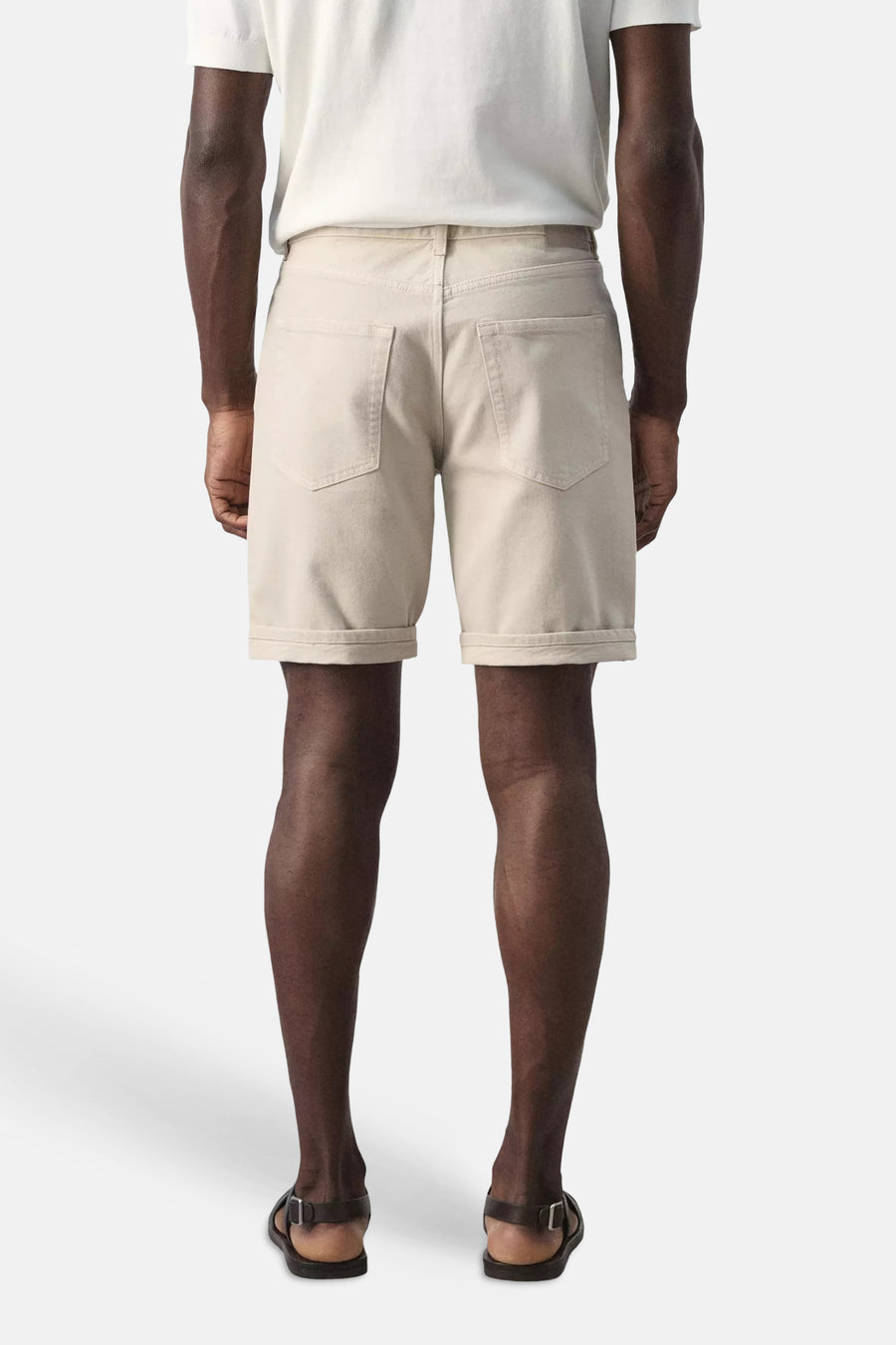 Beige Bermuda van MANGO, van achteren gezien, met opgerolde zomen en achterzakken, gedragen met een wit T-shirt en sandalen.