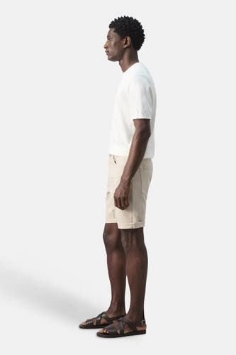Bermuda beige de MANGO, porté par un homme en t-shirt blanc et sandales marron foncé, vu de côté.