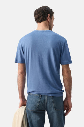 Blauw T-shirt met korte mouwen van MANGO, gezien van achteren, met jeans en een jas in de hand.

