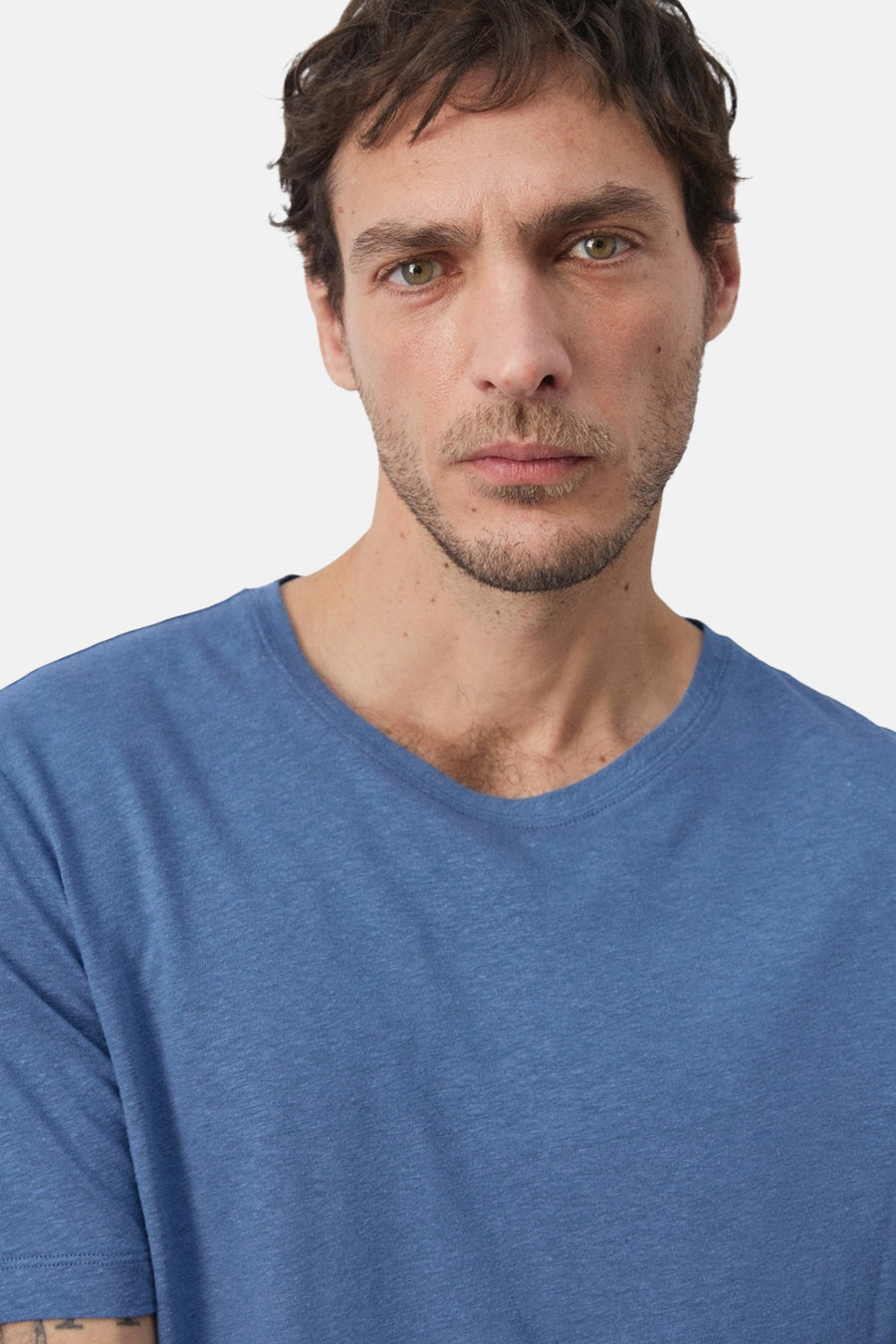 T-shirt bleu à manches courtes de MANGO, gros plan sur un homme avec une barbe de trois jours et un t-shirt bleu uni.