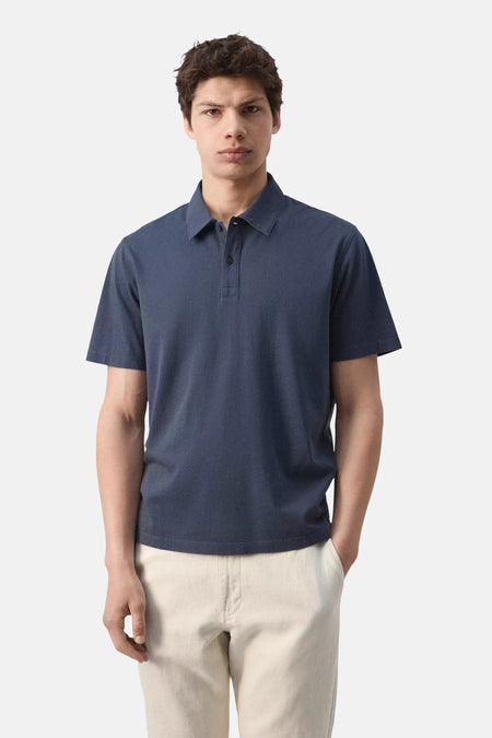 Polo bleue de MANGO à manches courtes et deux boutons, portée par un homme avec un pantalon clair.