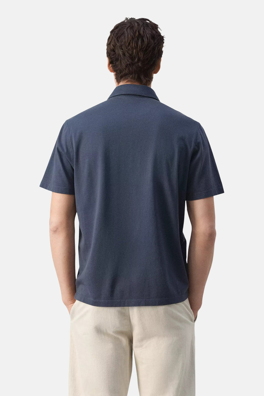 Blauwe polo van MANGO met korte mouwen, gedragen door een man in lichte broek, rugaanzicht.