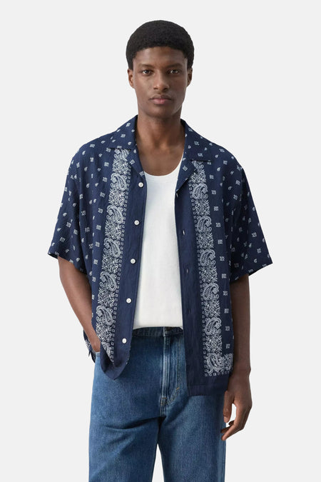 Chemise bleue à manches courtes de MANGO, avec motifs cachemire et géométriques blancs, vue de dos, portée par un homme avec un jean.