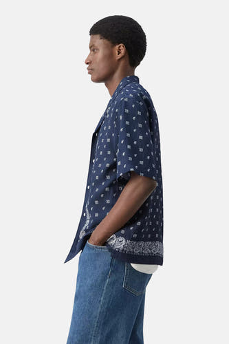 Blauw overhemd met korte mouwen van MANGO met wit bandana-patroon, gedragen door een man in jeans, zijwaarts.