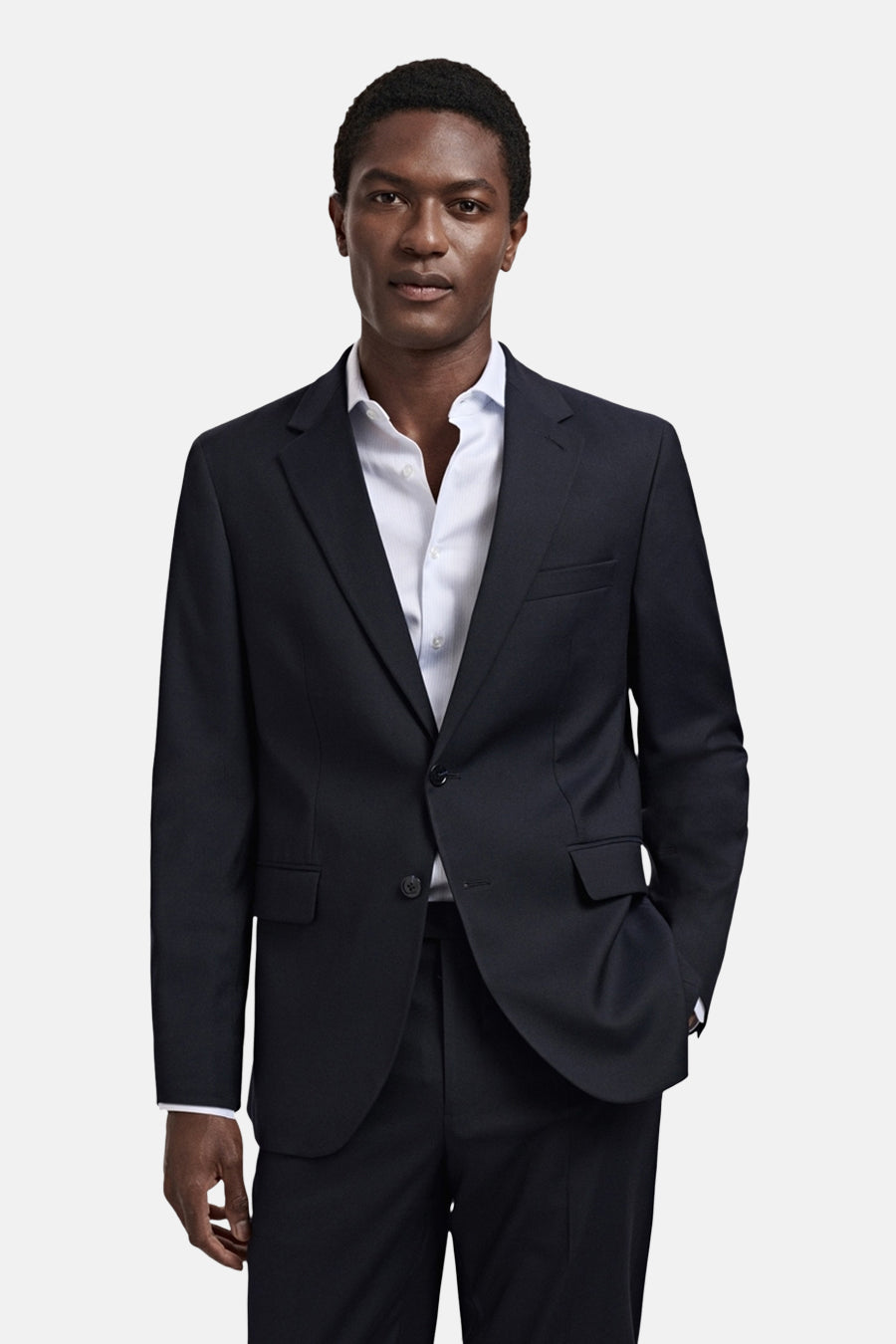 Blazer bleue de MANGO, avec une fermeture à boutons et une poche poitrine, portée avec une chemise bleu clair.