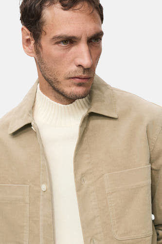 Chemise beige à manches longues de MANGO portée sur une veste crème.