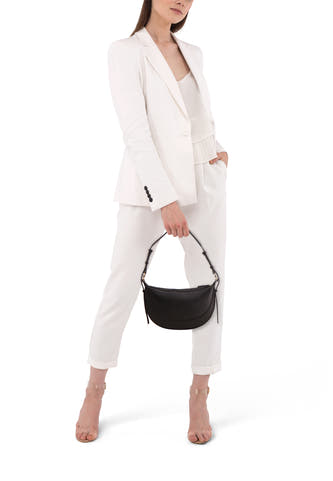 Zwarte schoudertas van MANGO, gedragen door een model in een witte broek en blazer.
