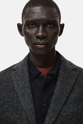 Multikleurige blazer van MANGO, met een subtiel patroon en een fijne textuur, gedragen over een donker shirt met een rode kraag.
