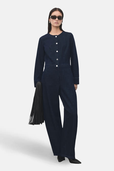 Combinaison de denim bleu marine de MANGO, avec des manches longues, une fermeture à boutons et des poches, associée à des chaussures noires.