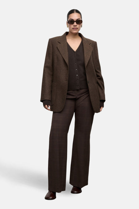 Vrouw draagt bruin tweed pak met zonnebril.