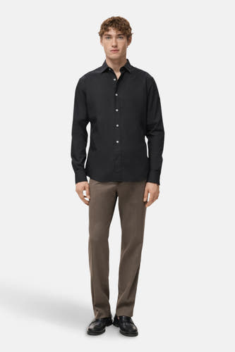 Chemise noire à longues manches de MANGO, avec un col classique et une fermeture à boutons, associée à des pantalons marron et des chaussures noires.