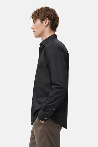 Chemise noire à longues manches de MANGO, vue de dos, portée avec un pantalon marron.