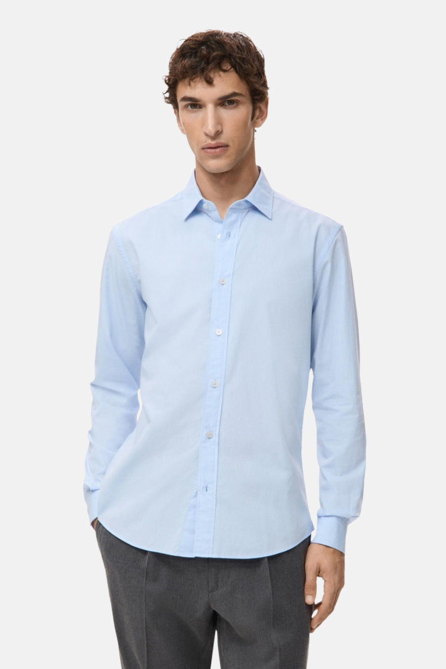 Chemise bleue à manches longues de MANGO, en tissu uni, portée avec un pantalon gris.
