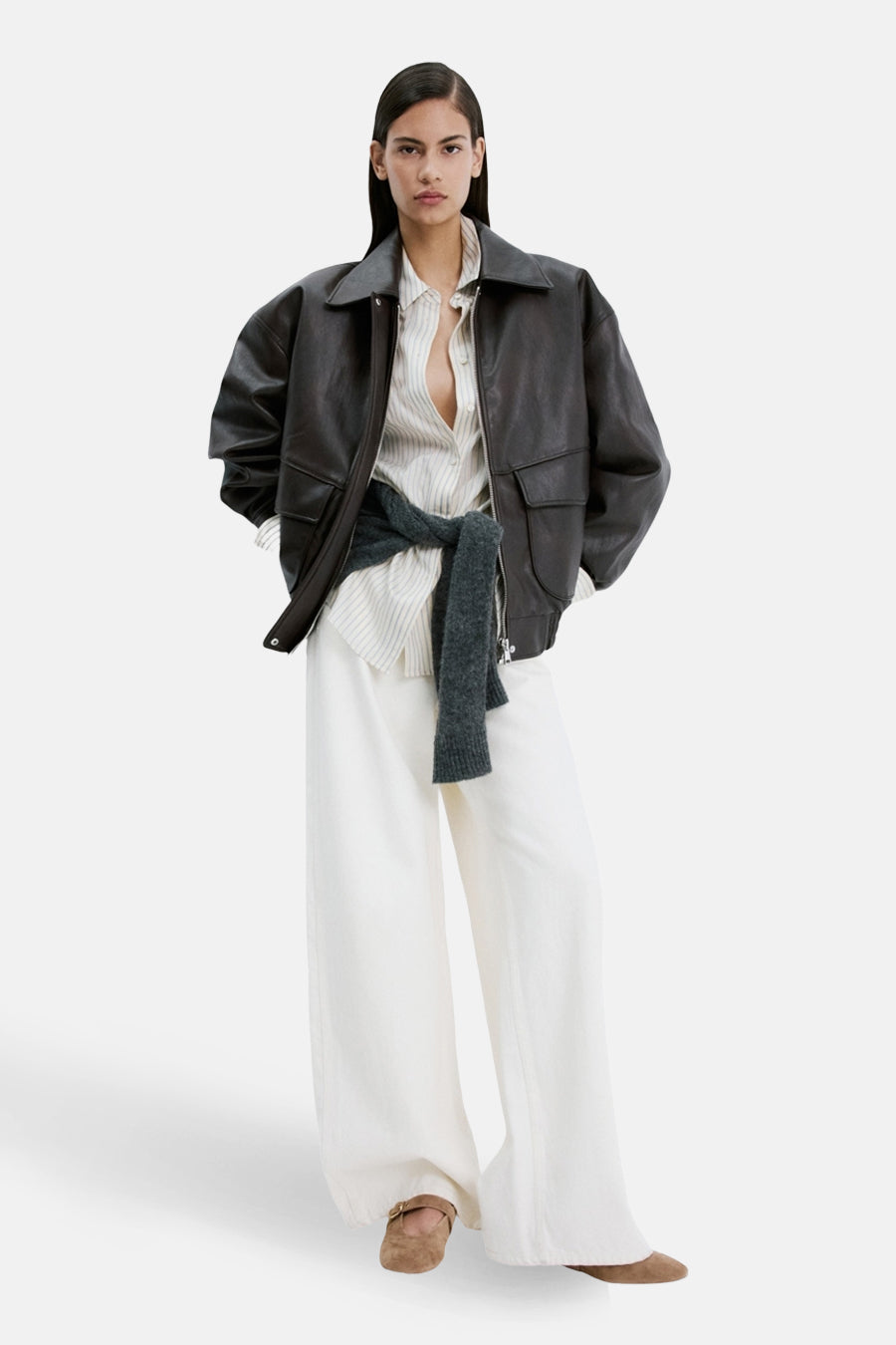 Bruine platte schoenen van Mango, gedragen door een model met een bruine leren jas, gestreept shirt en witte broek.
