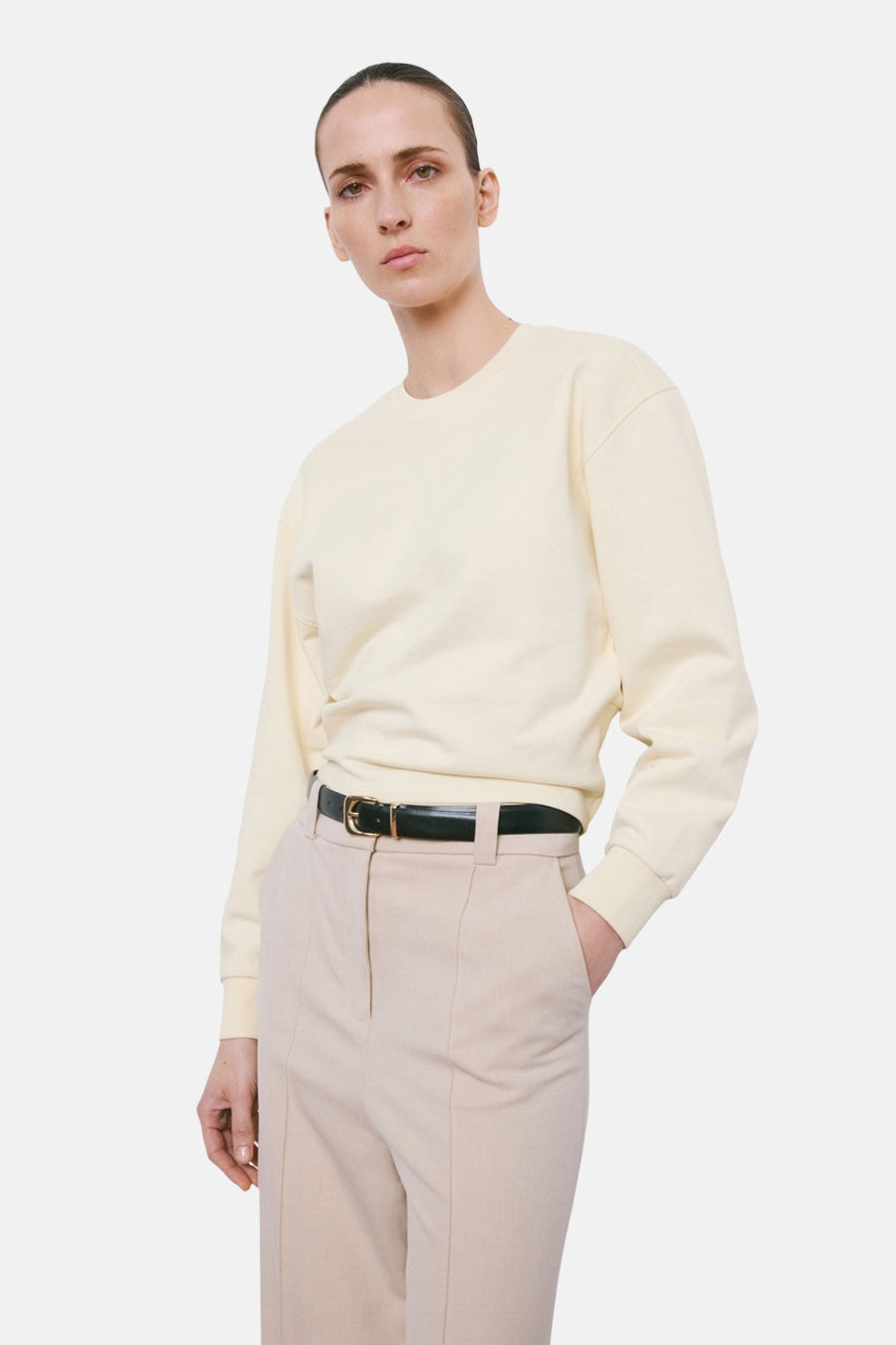 Beige sweater van MANGO, met lange mouwen en gedragen met een zwarte riem en beige pantalon.
