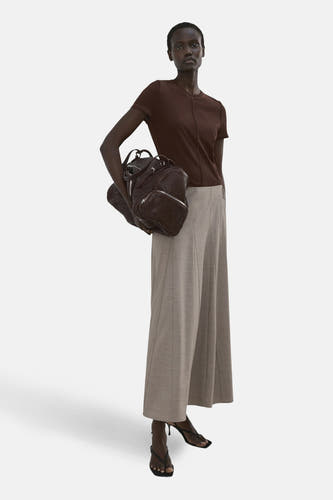 T-shirt marron à manches courtes de MANGO, avec couture centrale sur le devant, associé à un pantalon ample gris clair et des talons noirs.