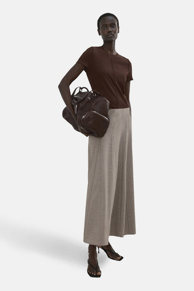 T-shirt marron à manches courtes de MANGO, avec couture centrale sur le devant, associé à un pantalon ample gris clair et des talons noirs.