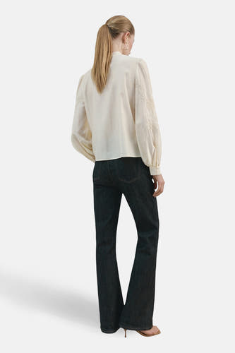Blouse écru à manches longues de MANGO, avec détails brodés sur les manches, combinée avec un jean foncé.