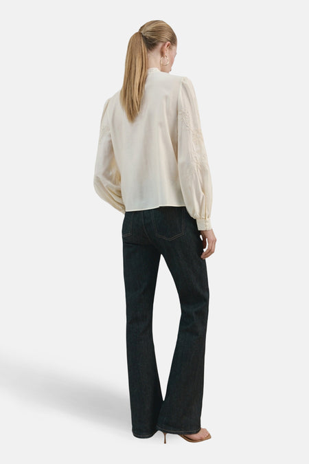 Ecru blouse met lange mouwen van MANGO, met geborduurde details op de mouwen, gecombineerd met donkere jeans.
