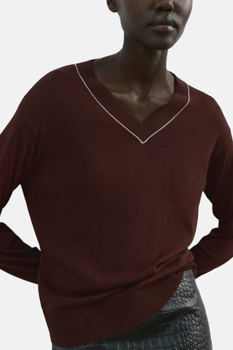 Pull marron à col en V de MANGO, avec manches longues et une mini-jupe noire ajustée à imprimé crocodile.