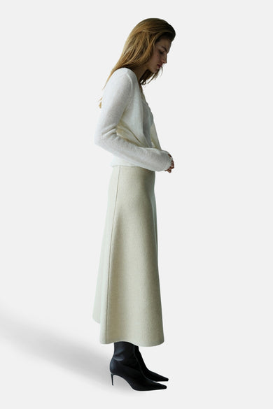 Gilet écru de MANGO, porté avec un pull blanc et une jupe beige, en vue de profil.