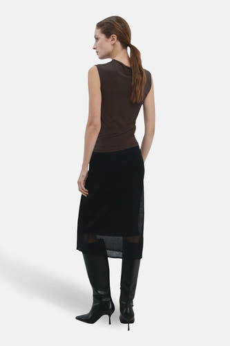 Mouwloze bruine blouse van MANGO, met een zwarte rok en zwarte leren laarzen met hak.