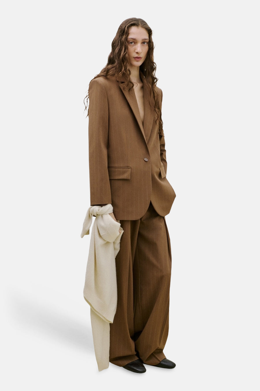 Blazer marron de MANGO avec un motif rayé, assortie à un pantalon assorti et une écharpe blanche à la main.