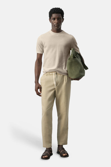 T-shirt beige à manches courtes de MANGO, porté avec un pantalon en coton léger et des sandales en cuir, avec un sac cabas vert.
