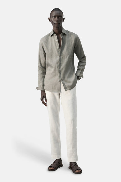 Chemise marron à manches longues de MANGO, portée avec un pantalon clair et des sandales marron.