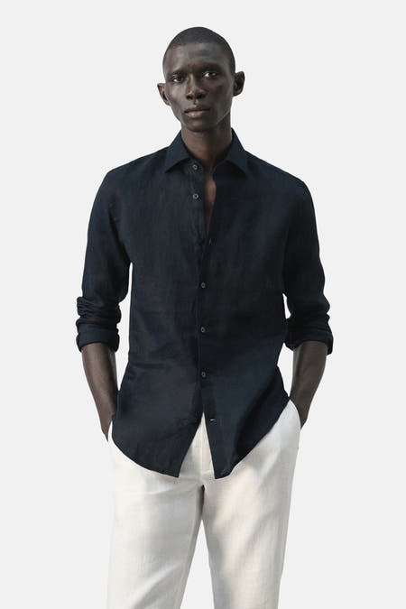 Chemise bleue à manches longues de MANGO, vue de dos avec une texture unie et un pantalon blanc.