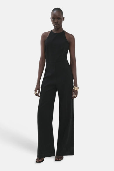Zwarte jumpsuit van MANGO met wijde pijpen, een halternek en gouden sieraden.
