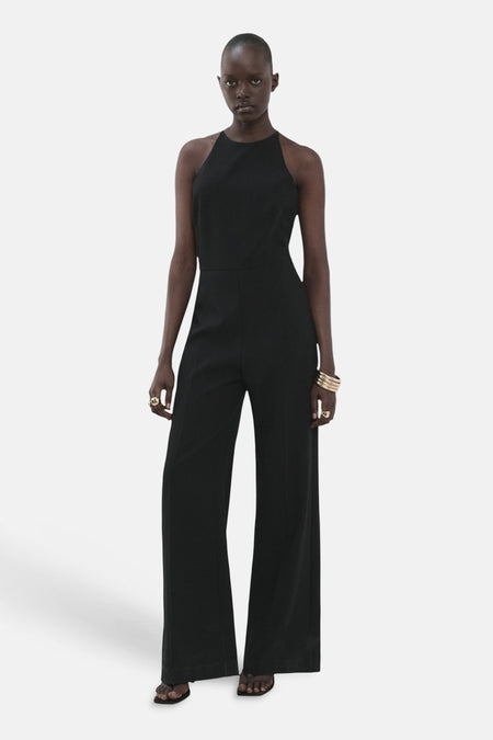 Zwarte jumpsuit van MANGO met wijde pijpen, een halternek en gouden sieraden.
