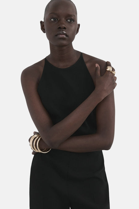 Zwarte jumpsuit van MANGO, met racerback halslijn en gouden armbanden en ringen als accessoire.