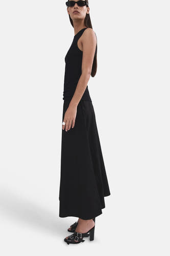 Lange zwarte rok van MANGO, gedragen door een model in zijprofiel met een tanktop en gespsandalen.