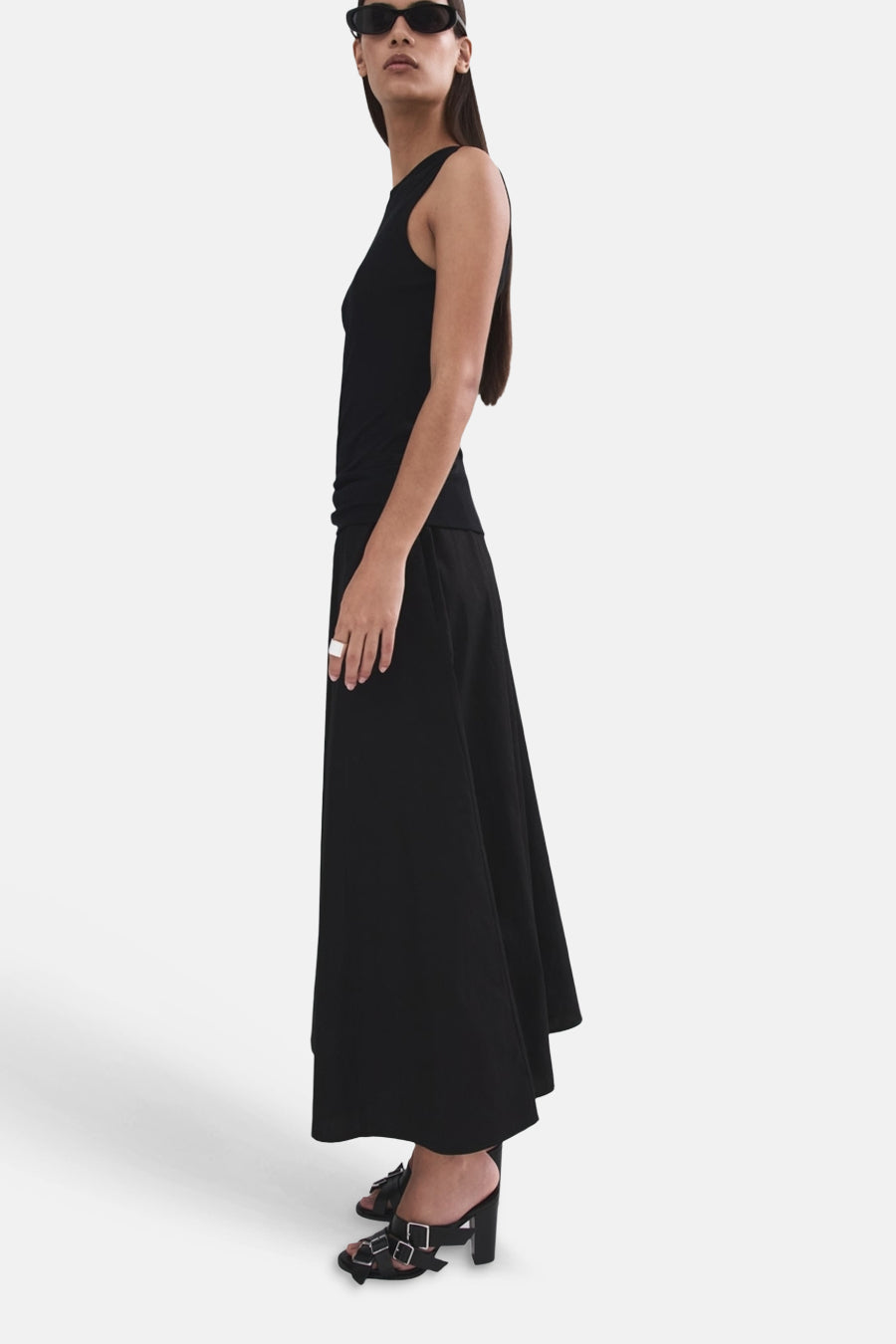 Lange zwarte rok van MANGO, gedragen door een model in zijprofiel met een tanktop en gespsandalen.