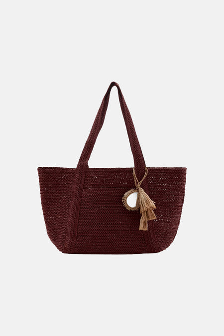 Bordeauxrode geweven schoudertas van MANGO met twee handvatten en een decoratieve hanger met spiegel en kwastjes.