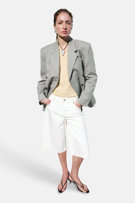 Witte Bermuda van MANGO met wijde pijpen en zichtbare stiksels, gedragen met een gele top, grijze blazer en zwarte sandaaltjes.