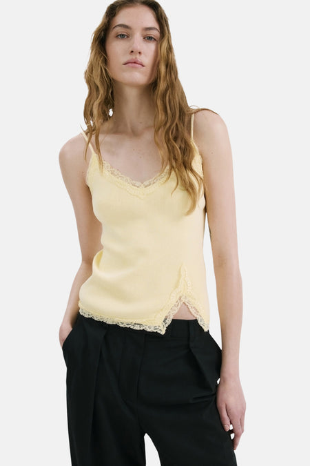 Gele spaghettibandjestop van MANGO met kanten V-hals en zijsplit, gedragen met zwarte broek.