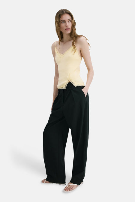 Gele spaghettibandjestop van MANGO met kanten details, gecombineerd met een donkere, wijde broek en lichte teenslippers.