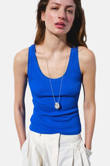 Blauwe geribbelde tanktop van MANGO, gedragen door een vrouw met witte broek en zilveren ketting.