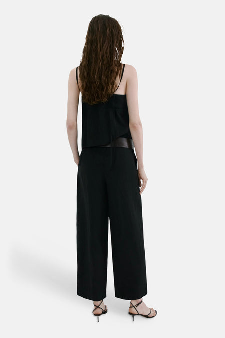 Wijdvallende zwarte broek van MANGO, van achteren gezien, gedragen met een zwarte top en sandalen.